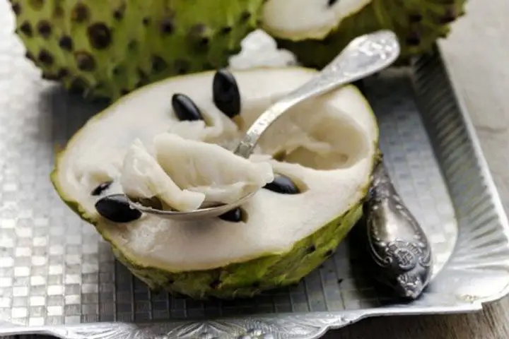 una cucharilla con pulpa de guanabana encima de fruto abierto