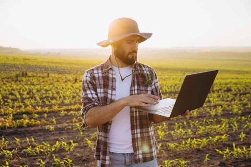 Agricultor joven usando inteligencia artificial en una laptop en un campo de cultivo al atardecer.