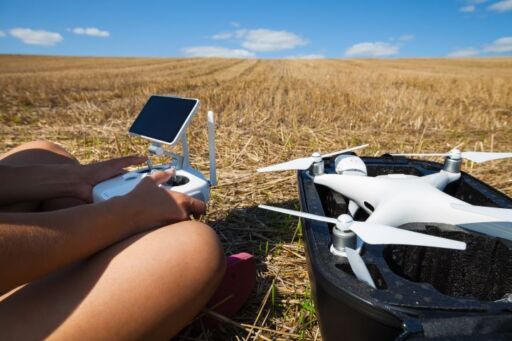 Operador utilizando un control remoto junto a un dron plegado en el campo para la gestión de drones en lecherías.